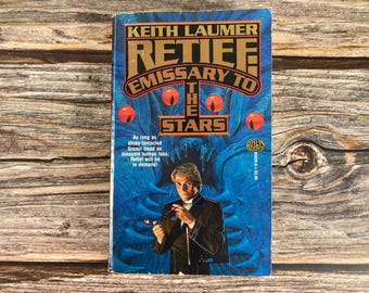May include: A science fiction paperback book cover with a blue and black background. The title is "Retief: Emissary to the Stars" by Keith Laumer. A man in a dark suit is standing in front of a large, tentacled creature with glowing eyes.