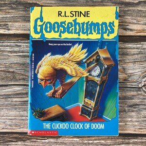 May include: A paperback book titled "Goosebumps: The Cuckoo Clock of Doom" by R.L. Stine. The cover features a yellow and blue design with a menacing bird perched on a clock. The Scholastic logo is at the bottom.