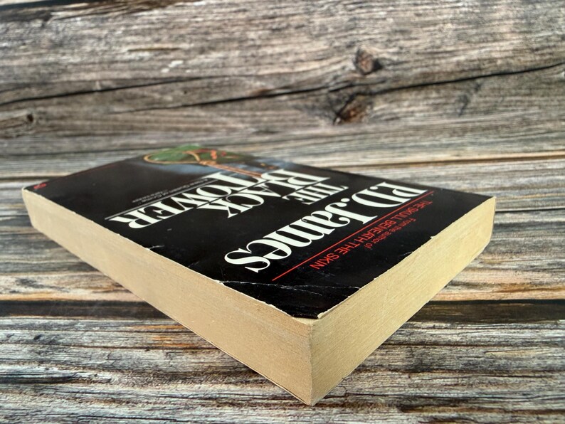 May include: A hardcover book titled "The Black Tower" by Ed James. The book has a black cover with white and red text. The book is lying on a wooden surface.