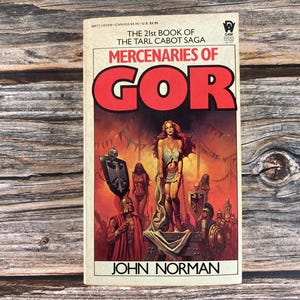 May include: A paperback book cover with a red and white illustration of a woman in a red dress and a sword. The title of the book is "Mercenaries of Gor" and the author is "John Norman".