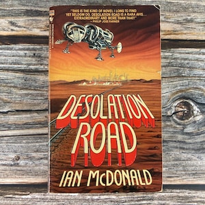 May include: A vintage paperback book cover with a futuristic illustration of a spaceship flying over a desert landscape. The title of the book is "Desolation Road" in red and white lettering. The author is "Ian McDonald".