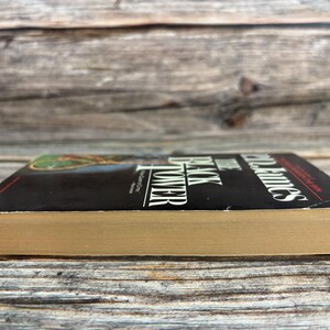 May include: A hardcover book with a black cover and the title "The Black Tower" by P.D. James. The book's pages are a light tan color. The book is set against a weathered wooden background.