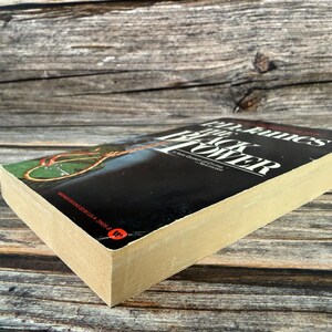 May include: A hardcover book titled "The Black Tower" by PD James. The book has a black cover with white text and a colorful illustration. The pages are yellowed with age, and the book is resting on a wooden surface.