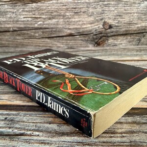 May include: A hardcover book titled "The Black Tower" by P.D. James. The book has a black cover with white lettering and a graphic of a noose and key. The book's pages are yellowed with age, and the cover shows some wear.