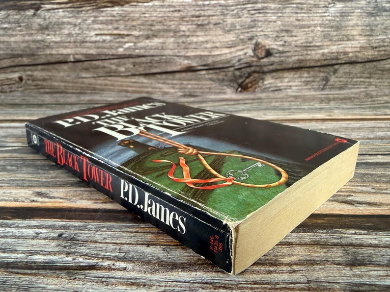 May include: A hardcover book titled "The Black Tower" by P.D. James. The book has a black cover with white lettering and a graphic of a noose and key. The book's pages are yellowed with age, and the cover shows some wear.