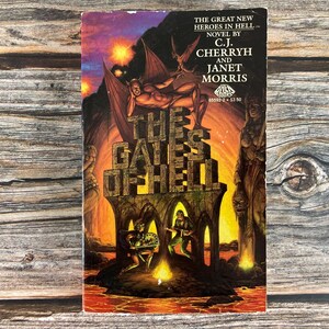 May include: Vintage paperback book titled "The Gates of Hell" by C.J. Cherryh and Janet Morris. The cover art features a fiery scene with demonic figures and the title in large, stylized letters. The book is set against a wooden background.