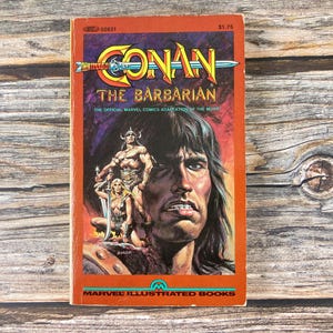 May include: Vintage comic book cover for "Conan the Barbarian," featuring a muscular warrior and a woman with a sword. The title is in yellow and blue, set against an orange background. The Marvel Illustrated Books logo is at the bottom.