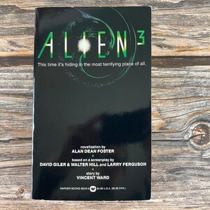 May include: A black and green book cover with the title "Alien 3" in white text. The tagline reads "This time it's hiding in the most terrifying place of all." The cover also includes the names of the authors and the publisher.
