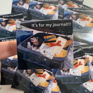 May include: A square sticker featuring a photograph of an opossum inside a dark gray trash bin filled with various items including a MetroCard, a red ribbon, and paper scraps. The text "It's for my journal!!!" is printed in white at the top.