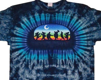 May include: A tie-dye t-shirt in shades of blue and black. The shirt features a central oval design with dancing bear silhouettes in various colors under a crescent moon and stars. The shirt is a classic crew neck style.
