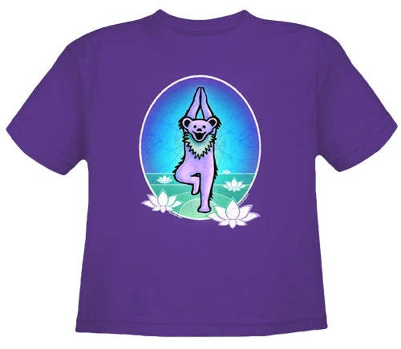 May include: Purple t-shirt with a graphic of a cartoon bear in a yoga pose. The bear is surrounded by lotus flowers and a blue and green background.
