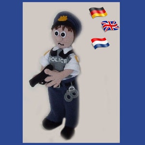 May include: A crocheted police officer doll wearing a blue uniform with a black gun and handcuffs. The doll has brown hair and brown eyes. The doll is standing on a white background with flags of Germany, the United Kingdom, and the Netherlands in the background.