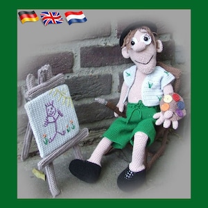 Może przedstawiać: Haftowany, pluszowy artysta trzymający paletę i pędzel, siedzący na krześle przed sztalugą z rysunkiem postaci.