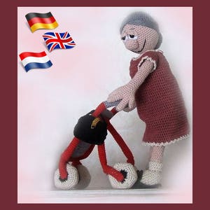 Może przedstawiać: Lalka szydełkowa z szarymi włosami i czerwoną sukienką pcha czerwony i czarny wózek inwalidzki z białymi kołami. Lalka uśmiecha się i ma przyjazny wyraz twarzy. W tle widoczne są trzy flagi: niemiecka, brytyjska i holenderska.