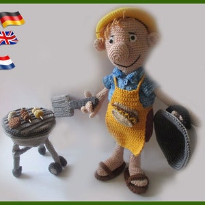Op de afbeelding: Een gehaakte pop met een gele schort en een blauw shirt, die een spatel en een grillpan vasthoudt. De pop staat naast een kleine grijze grill met eten dat erop kookt.