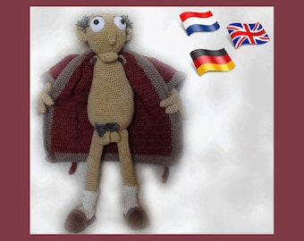 May include: A crocheted doll wearing a burgundy and beige robe. The doll has a brown beard, brown hair, and large black eyes. The doll is standing on a white background with flags of the Netherlands, the United Kingdom, and Germany in the background.