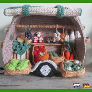 May include: A crocheted miniature market stall in shades of pink, beige, and green, filled with crocheted produce. The stall features a shelf with miniature vegetables and bottles, and baskets overflowing with crocheted vegetables.