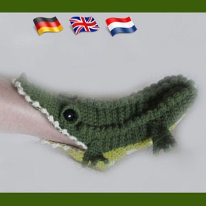 May include: Green crocheted alligator slipper with a white crocheted trim and a black eye. The slipper is being worn on a person's foot.