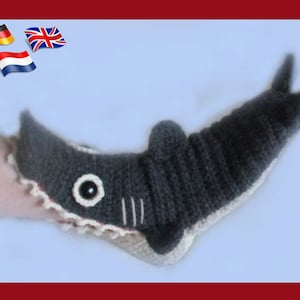 May include: Gray crocheted shark slipper with a white crocheted mouth and a black eye. The slipper is worn on a person's foot.