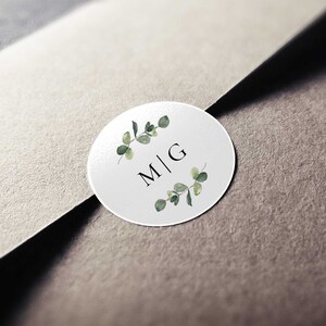 May include: White round sticker with a green leafy wreath and the initials "M|G" in black.