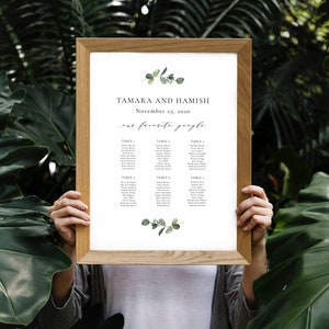 Puede incluir: Un plano de asientos de boda con un diseño simple y moderno. El plano está impreso en papel blanco y presenta una ilustración de hoja de eucalipto. El texto dice "Tamara y Hamish, 23 de noviembre de 2020, nuestra gente favorita". El plano enumera los nombres de los invitados asignados a cada mesa.