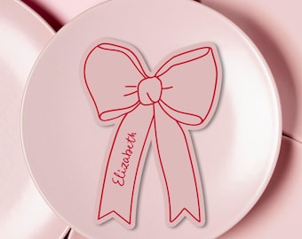 May include: Pink bow with a red outline and the name "Elizabeth" written on the ribbon.