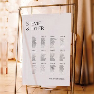 Könnte beinhalten: Ein weißer Hochzeitssitzplan mit goldenem Rahmen. Der Plan listet die Namen der Gäste auf, die den einzelnen Tischen zugeordnet sind, die von 1 bis 12 nummeriert sind. Der Plan ist mit "Stevie & Tyler" betitelt und enthält den Hashtag "#StevieAndTyler2025".