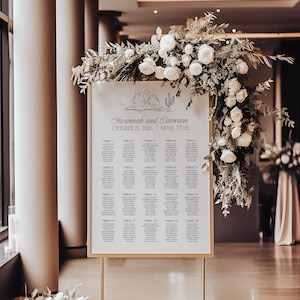 May include: A white wedding seating chart with a gold frame and a desert landscape illustration. The chart lists table numbers and guest names for a wedding on 21 October 2026, in Moab, Utah.
