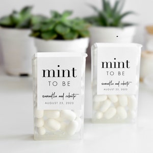 May include: Two clear plastic containers filled with white mints. Each container has a white label with black text that reads "mint to be" and the names "samantha and roberto" and the date "AUGUST 23, 2023".