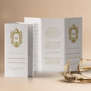 May include: A tri-fold wedding program with a gold crest featuring the letter "M" on the front cover. The program includes the names of the bride and groom, Maryanne Howard and Jackson Millner, the wedding date, and the location. The program also includes a thank you message, a section for the wedding party, and a section for the ceremony.