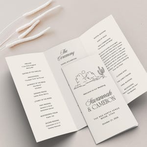 May include: A wedding ceremony program with a simple line drawing of a desert landscape. The program lists the order of events for the ceremony, including the prelude, processional, and readings. The program also includes the names of the bride and groom, Savannah & Cameron, and the date and location of the wedding, October 21, 2026, The Red Earth Venue, Moab, Utah.