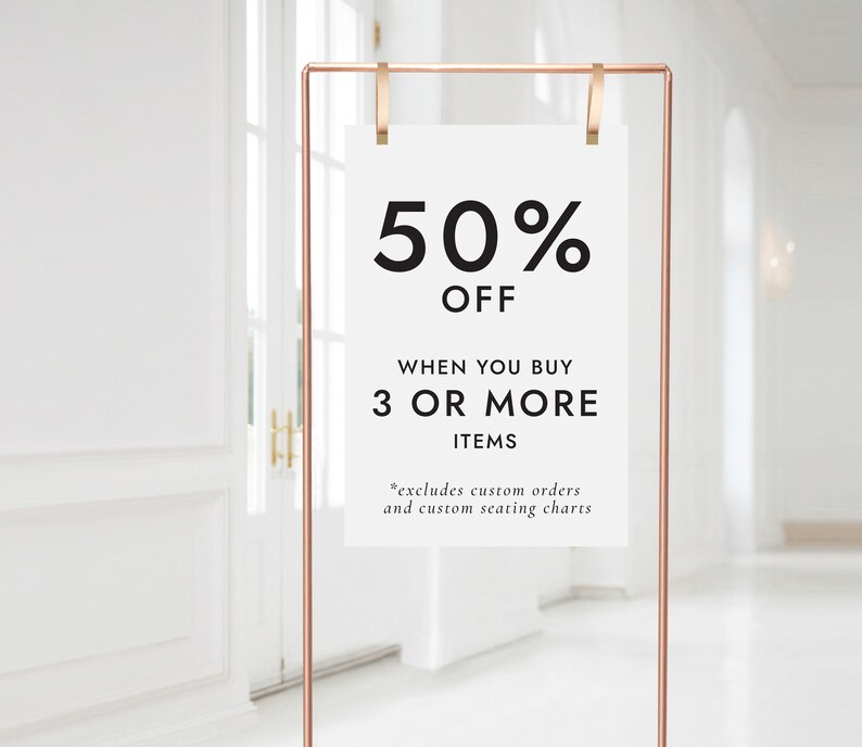May include: A white sign with a copper frame and clips, announcing a 50% off sale when you buy 3 or more items. The sign reads "50% OFF WHEN YOU BUY 3 OR MORE ITEMS *excludes custom orders and custom seating charts".