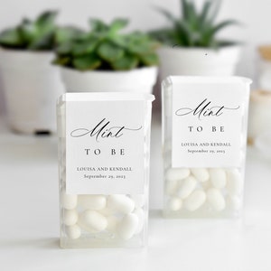 May include: Two clear plastic boxes filled with white mints. Each box has a white label with the words "Mint to Be" in elegant script, along with the names Louisa and Kendall and the date September 29, 2023.