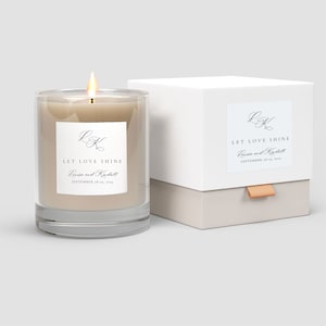 May include: A lit candle in a clear glass container with a white label that reads "LET LOVE SHINE" and the names "Louise and Kendall" and the date "SEPTEMBER 18-19, 2015". The candle is next to a white box with a matching label.