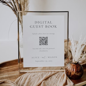 May include: A white sign in a gold frame with the text "DIGITAL GUEST BOOK" and a QR code. The text below the QR code says "Scan the code, enter the password aliceandmasonz". Below that is the text "ALICE & MASON September 29, 2025".