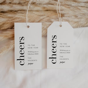 May include: Two white gift tags with black text that reads "cheers" and "To the New Year Wishing you a fabulous 2025 The Halberts xoxo".