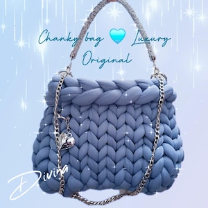 May include: A light blue chunky bag with a braided top and silver chain straps. The bag has a heart-shaped charm and the text "Chunky bag, Luxury, Original" is visible. The bag is made of a soft, knitted material.