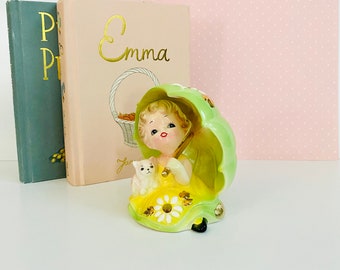 Peut inclure: Une figurine en céramique vintage d'une fille tenant un parapluie et un petit chien blanc. Elle porte une robe jaune à motif de marguerites vertes et blanches. La figurine est en position assise et a un parapluie vert.