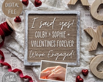 May include: A white letter board with the text "I said yes! Colby + Sophie = Valentines Forever Were Engaged!"  The board is surrounded by red hearts, lace, and wooden letters that spell "XO".
