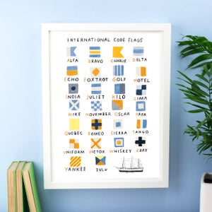 Peut inclure: Une impression encadrée blanche avec le titre "International Code Flags" et un tableau de 26 drapeaux avec leurs noms de lettres correspondants. Chaque drapeau est illustré avec un design simple en bleu, jaune et blanc.