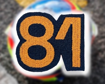 May include: A close-up of a navy blue and gold embroidered patch with the number "81" on it.