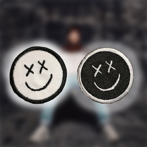 May include: Two embroidered iron-on patches in the shape of a smiley face with X's for eyes. One patch is white with black stitching and the other is black with white stitching.