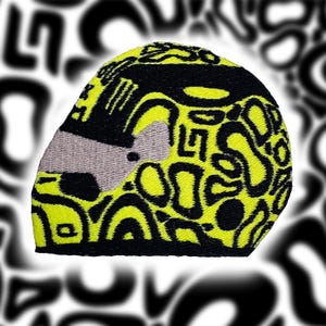 May include: A black and neon yellow embroidered helmet with a gray visor. The helmet features a repeating pattern of black shapes on a neon yellow background. The visor is gray and the helmet is set against a blurred black and white background.
