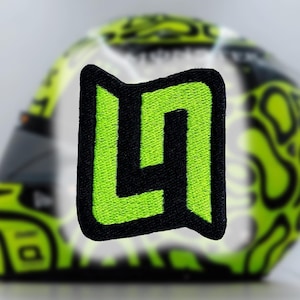 May include: A black and green embroidered patch with the letter "L" in a stylised font.