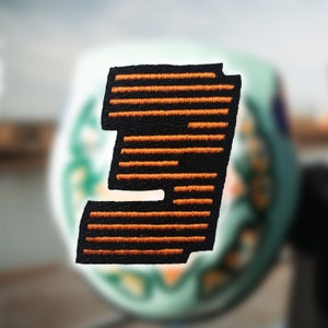 Puede incluir: Parche de fieltro negro con un gran número naranja "3" bordado en un patrón de rayas.