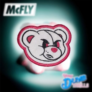 May include: A white embroidered patch of a cartoon bear with a pink nose and angry eyes. The bear is outlined in a dark pink thread and is set against a white background.
