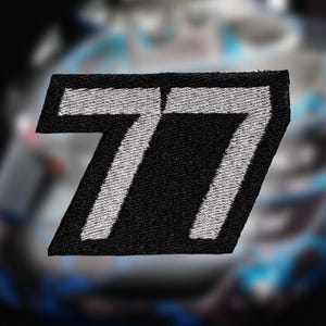 May include: A rectangular embroidered patch featuring the number 77 in a bold, slanted font. The design consists of white thread for the numerals set against a solid black background, with a thick black border framing the entire shape.