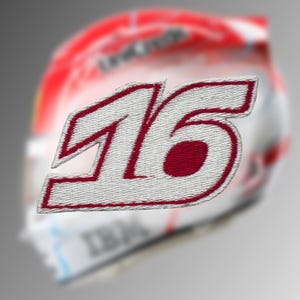 May include: Embroidered patch featuring the number "16" in white with a red outline and filling. The patch has a textured appearance, suggesting a fabric material. The background is blurred, showing a racing helmet.