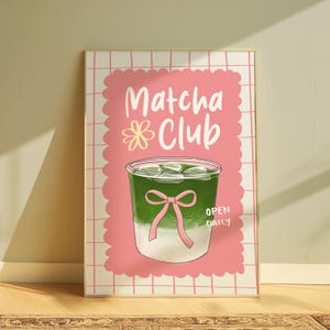 May include: A framed print featuring a matcha drink illustration. The artwork showcases a green beverage with ice cubes in a clear glass, adorned with a pink bow. The words "Matcha Club" are written in white, with "Open Daily" below.
