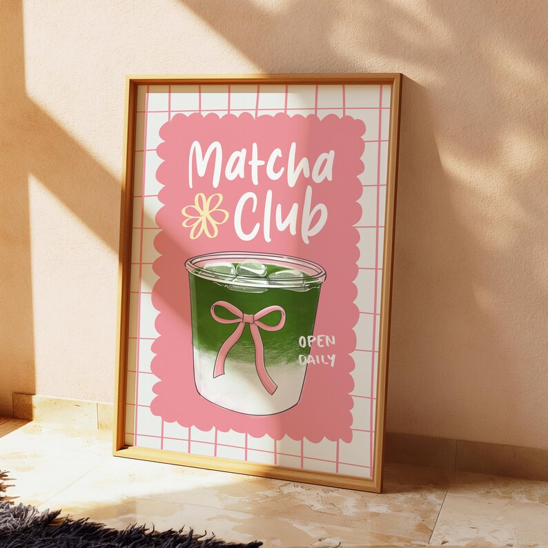 May include: A framed poster with a pink background and the words "Matcha Club" in white script. The poster features a green drink with ice cubes and a pink bow, with the words "Open Daily" below.